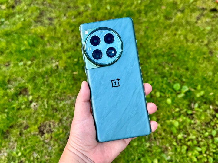 OnePlus 12 Flowy Emerald sostenido en la mano sobre fondo de hierba.